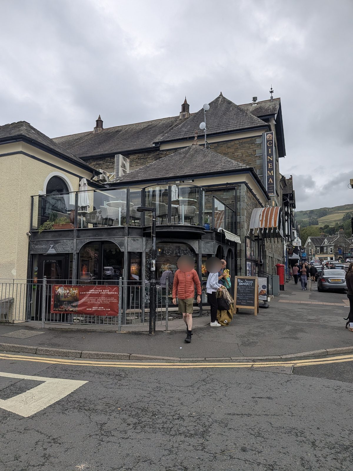A corner building in Ambleside with a cinema sign on the roofline, a first-floor balcony and a restaurant entrance at street level