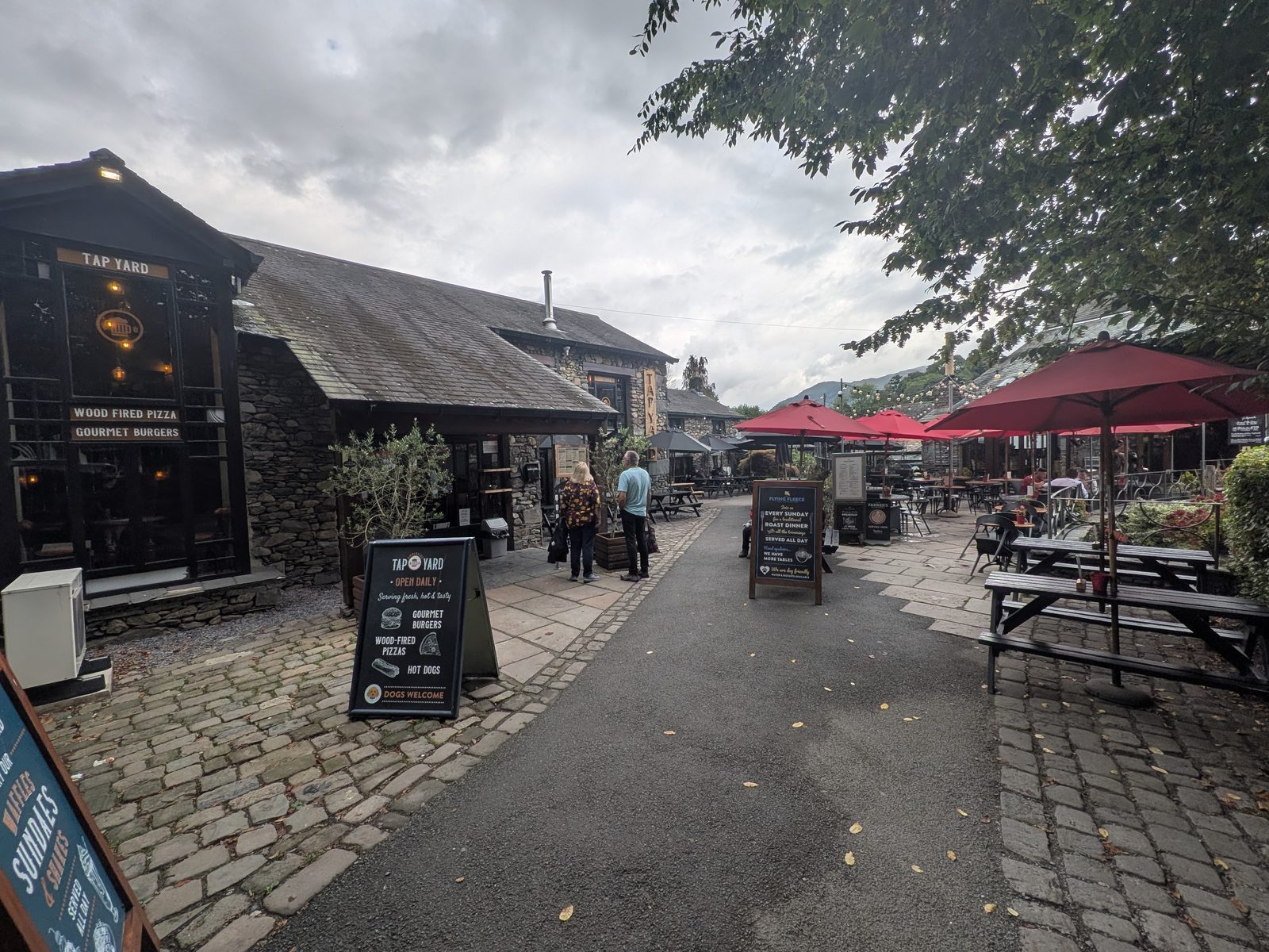 A cobbled lane of cafés and bars in Ambleside, with red parasols over outdoor tables and chalkboard menus by the doors