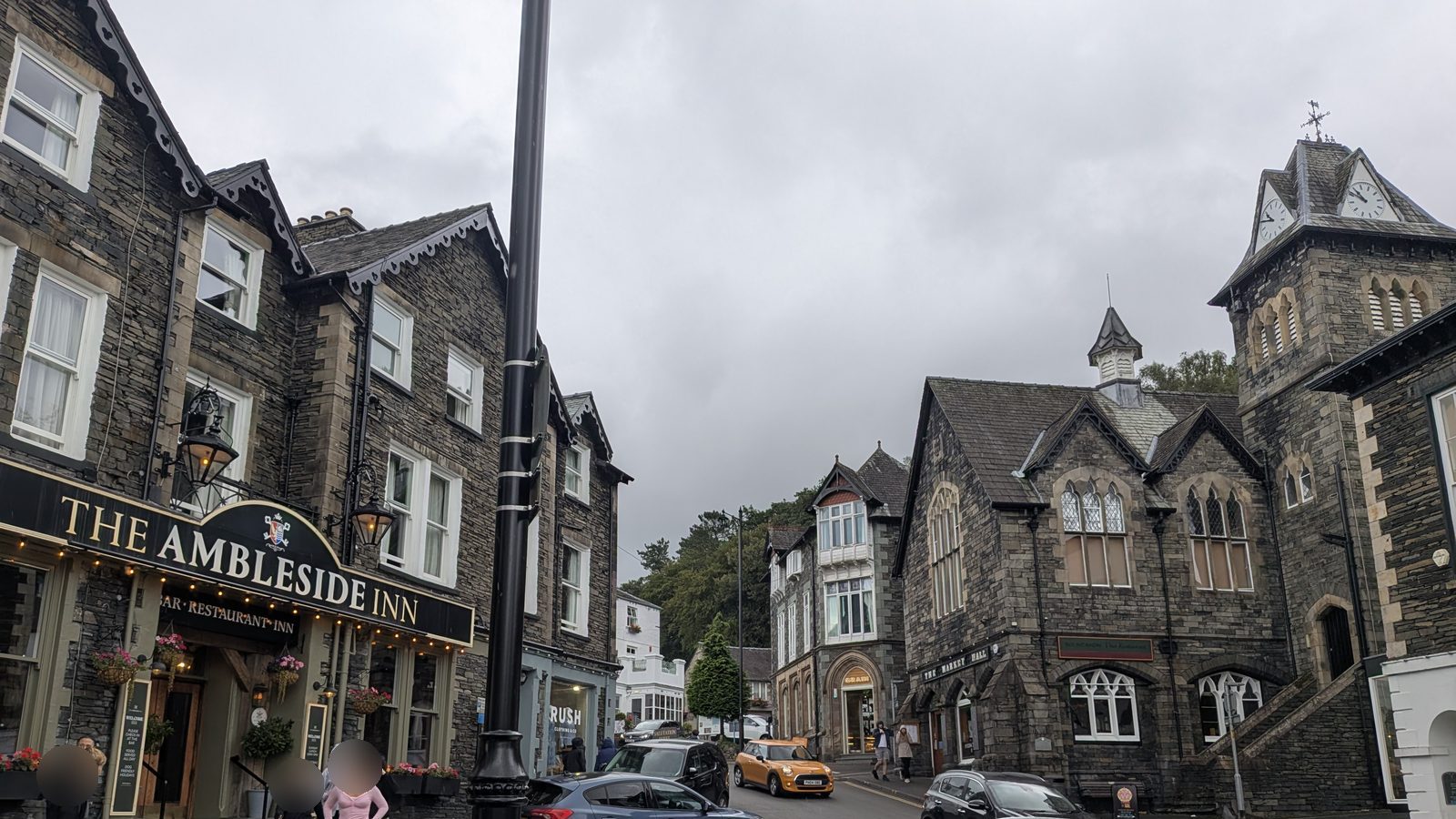 A pub on the corner of a slate-fronted street in Ambleside, with a gabled stone hall and clock tower further along