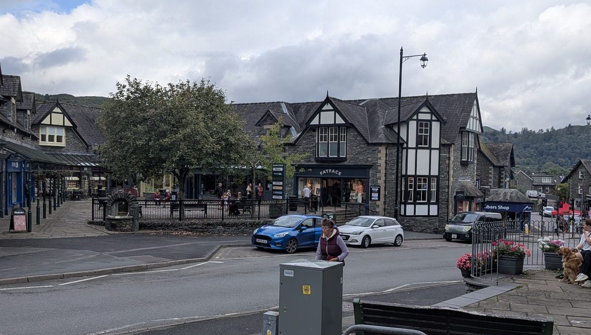 The square in Ambleside town centre: a black-and-white timbered building, a shelter, parked cars and people crossing the road