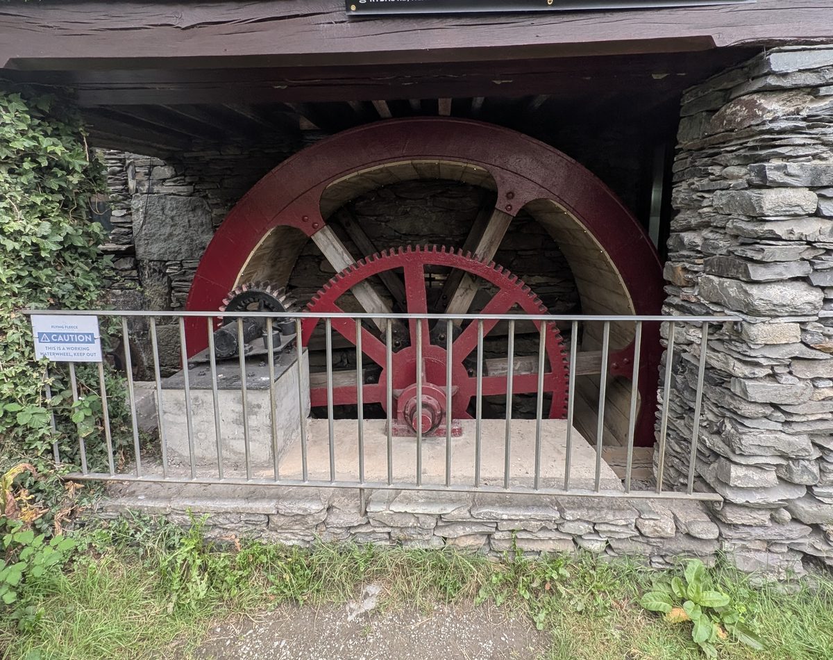 A red working waterwheel behind iron railings in a stone-walled recess, ivy on the wall above, Ambleside