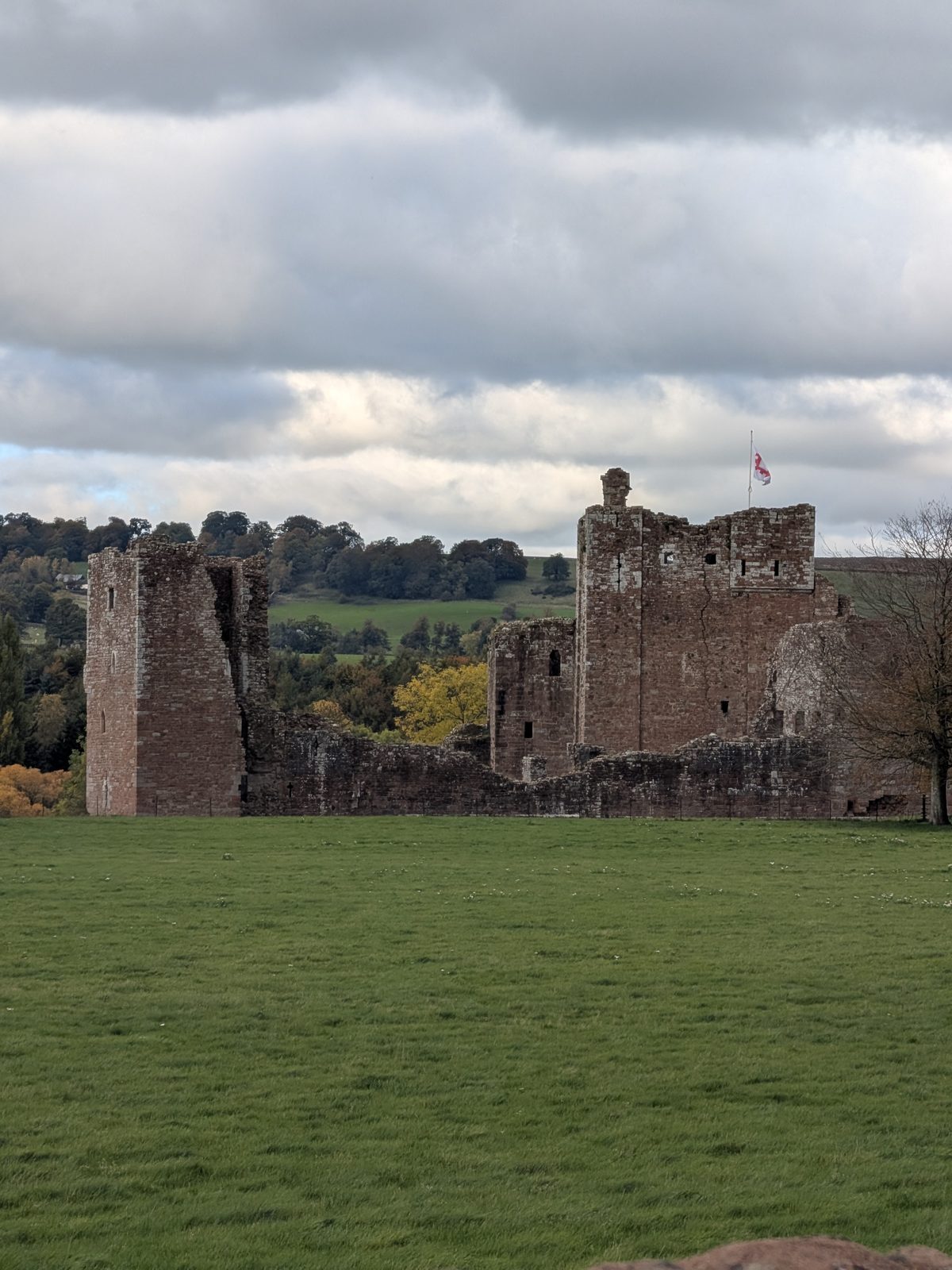 The tall red sandstone keep of Brougham Castle and its ruined walls across a green field, with a flag flying