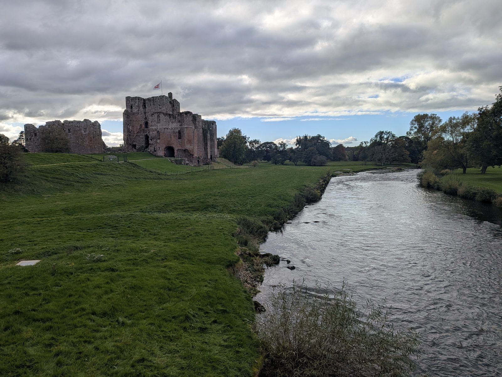 Brougham Castle's red sandstone keep and ruins seen across the River Eamont near Penrith