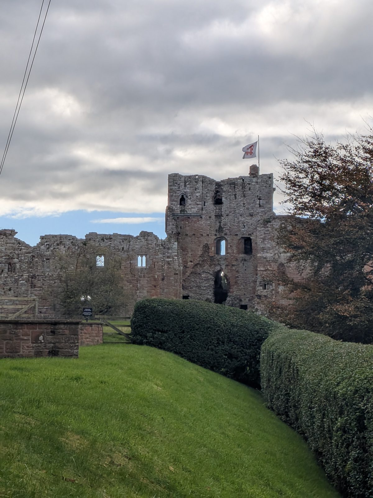 The gatehouse of Brougham Castle above a clipped hedge and a grass bank