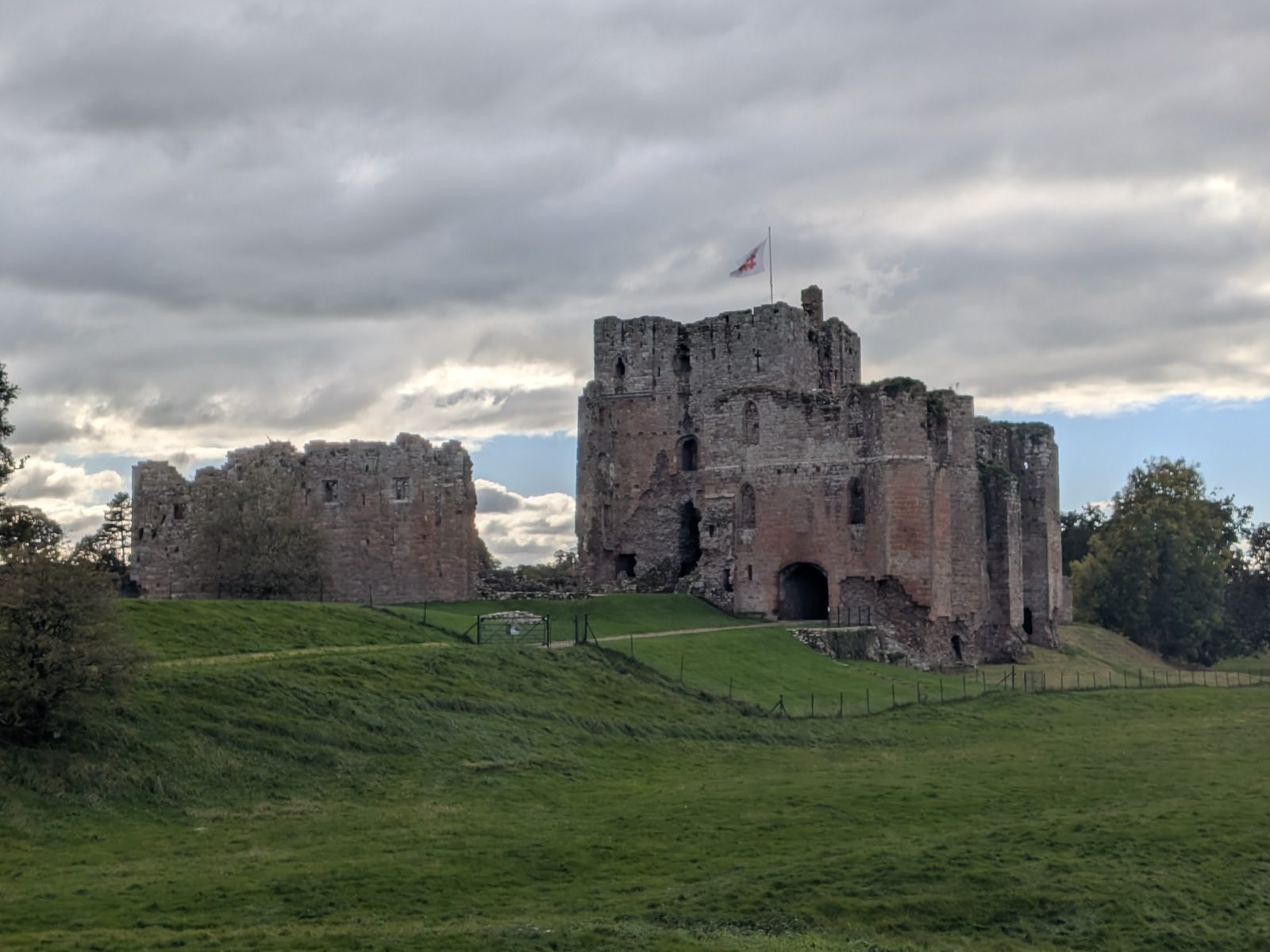 The ruined keep and gatehouse of Brougham Castle on a grass bank, with a flag flying from the keep