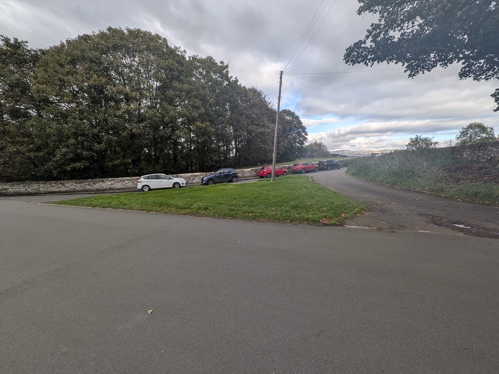 Cars parked along a stone wall on the dead-end triangle by the bridge at Brougham Castle
