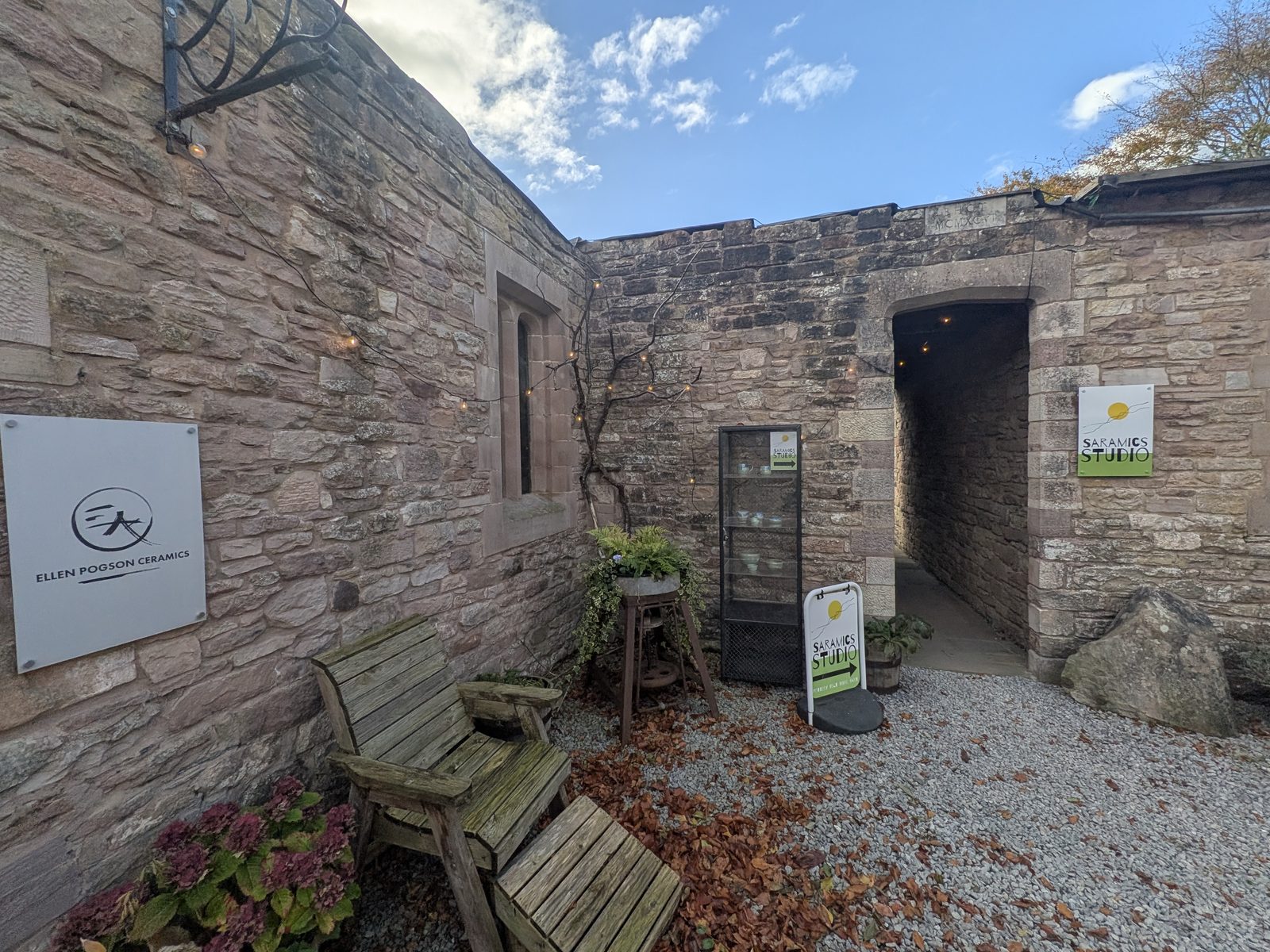 The Ellen Pogson Ceramics sign on a sandstone wall in a corner of the Brougham Hall courtyard, with a wooden bench