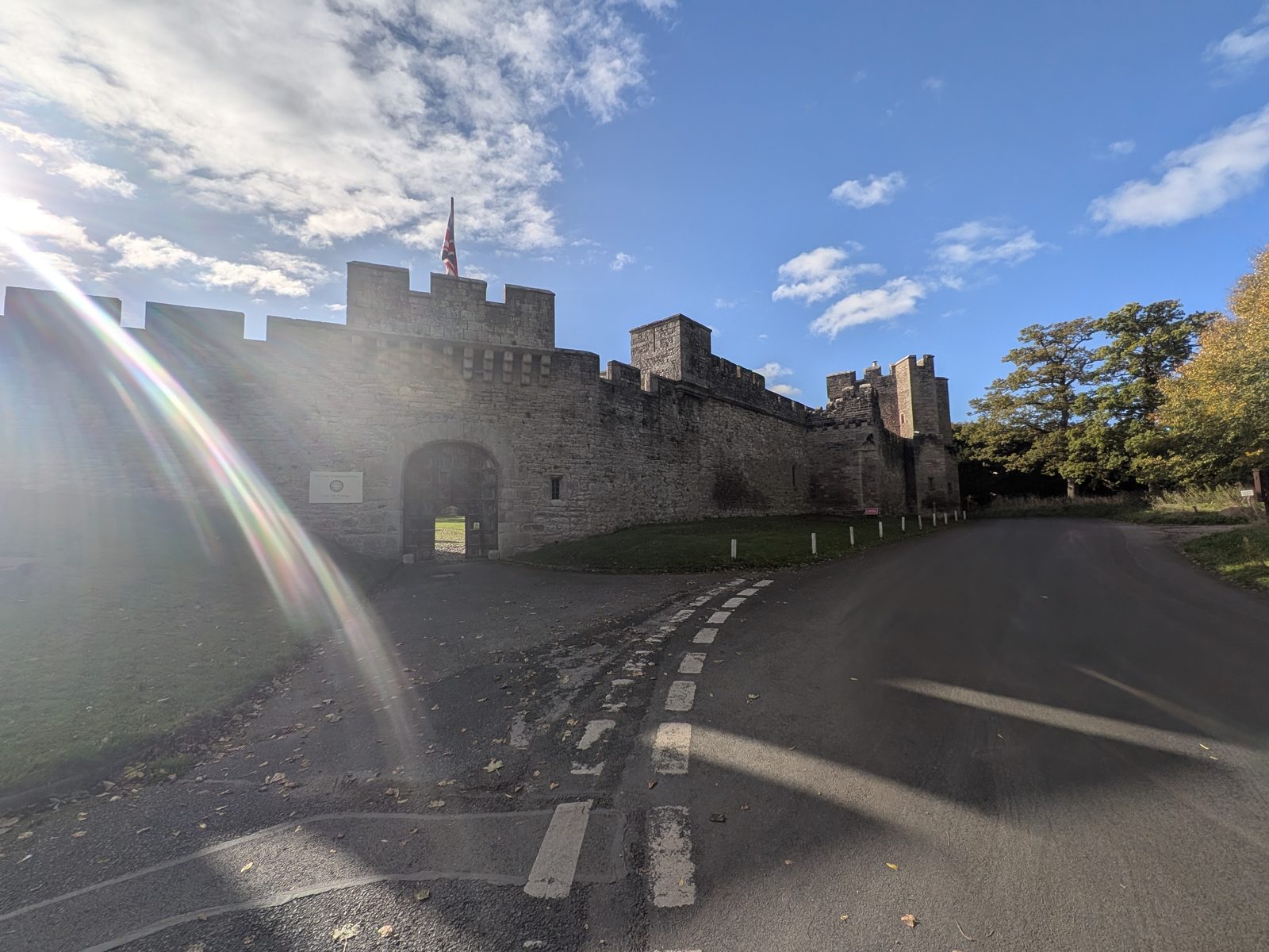 The battlemented sandstone gateway and walls of Brougham Hall beside the road, in low autumn sun