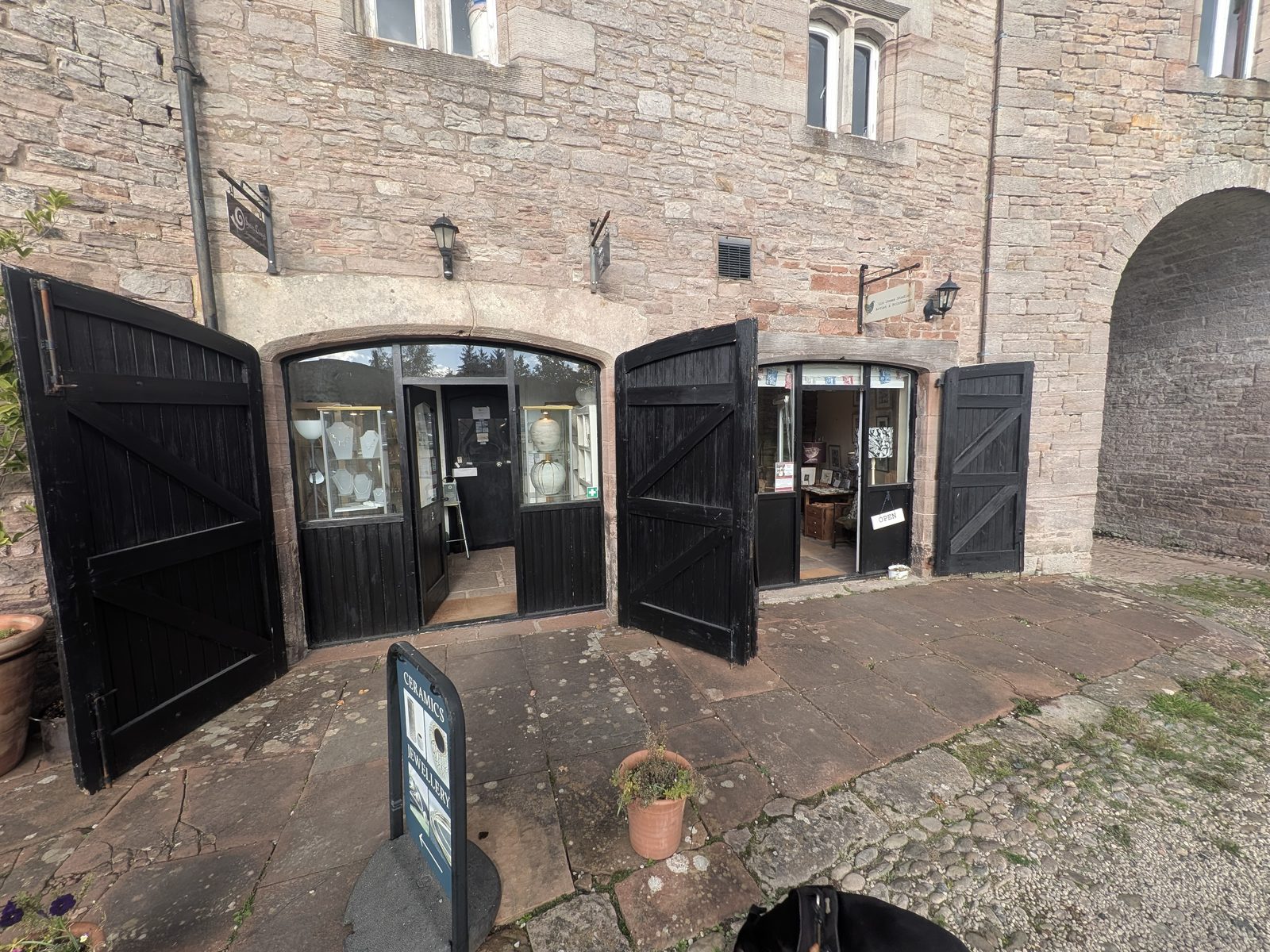 The black double doors of a pottery shop at Brougham Hall standing open onto the cobbled courtyard