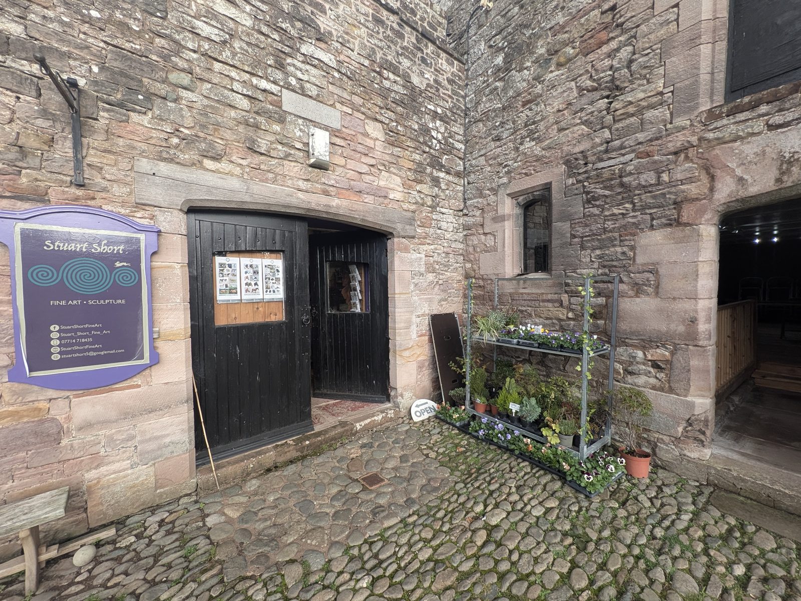 The door of Stuart Short's studio in the Brougham Hall courtyard, with his Fine Art and Sculpture sign and plants on the cobbles