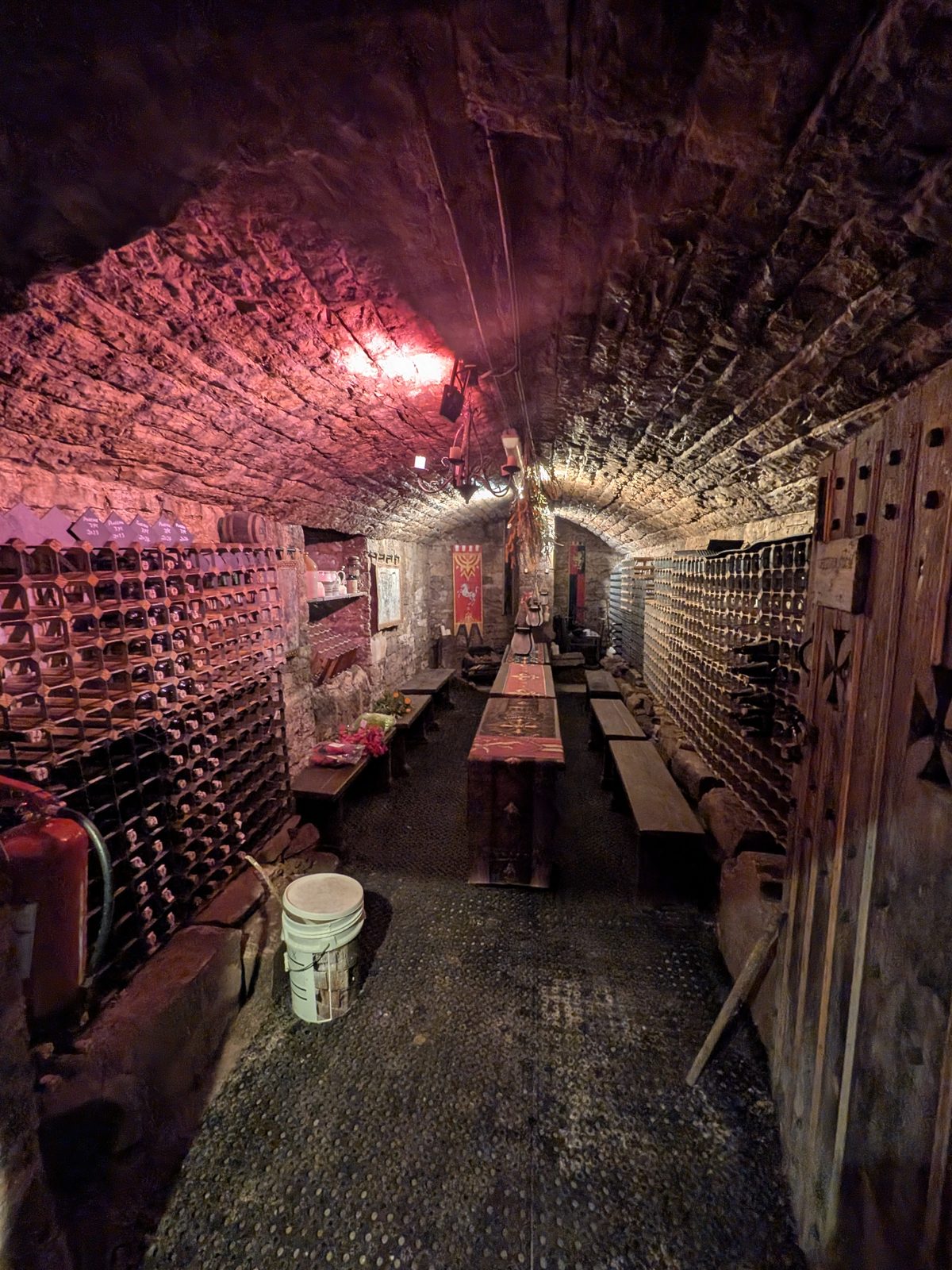 A brick-vaulted cellar at Brougham Hall lit in red, with racks of bottles along both sides and a long table