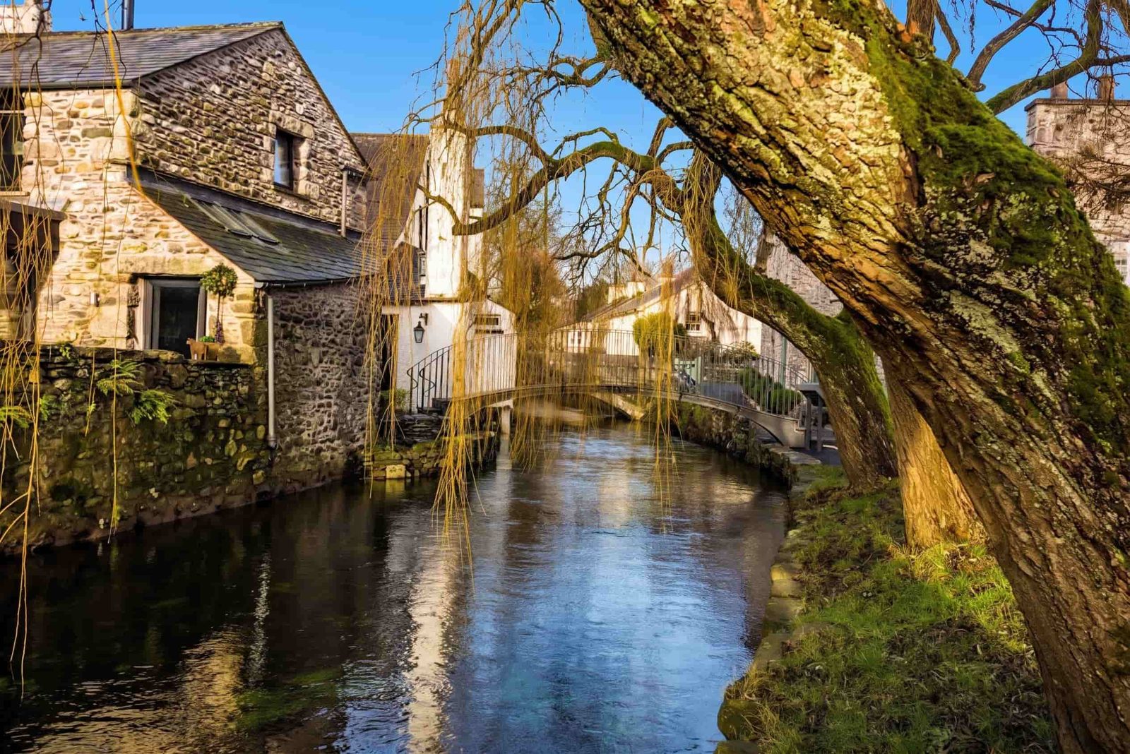 The beck and willow tree running through Cartmel village between stone cottages, Cumbria