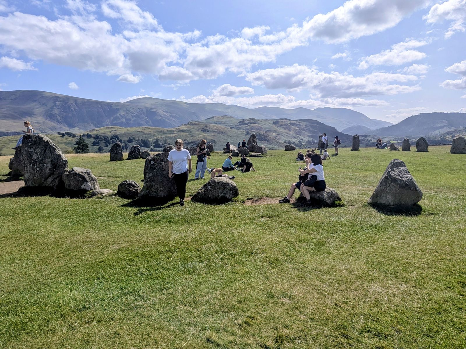 Visitors sitting among the stones at Castlerigg Stone Circle on a summer afternoon