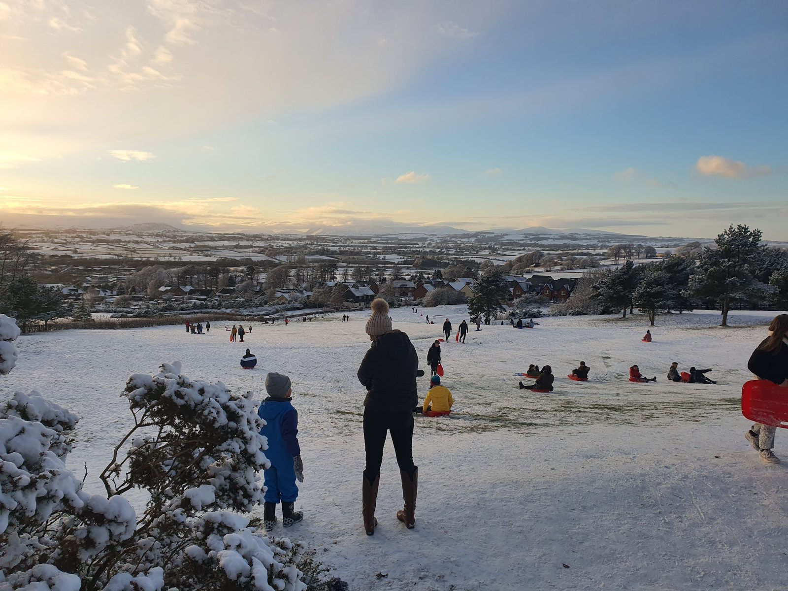 Families sledging on the snow-covered golf course above Penrith, the Eden valley white to the fells beyond under a low winter sun