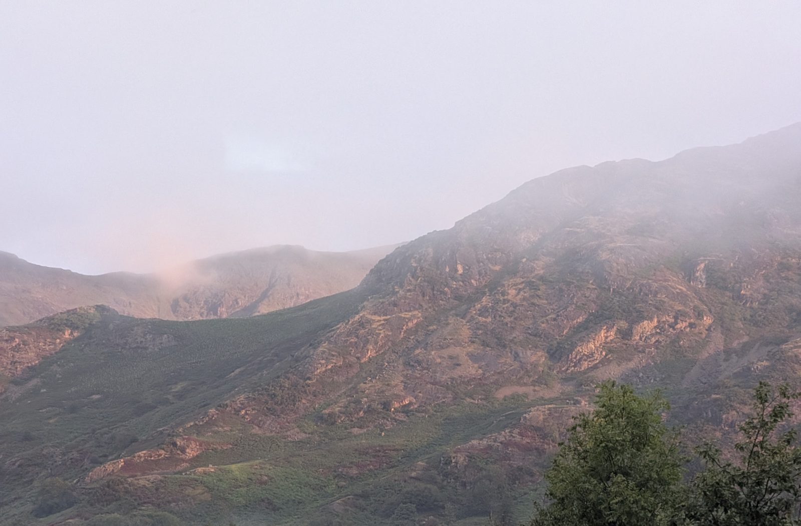 Rocky fellsides above Coniston at dusk, cloud sitting on the tops and a faint pink light on the crags