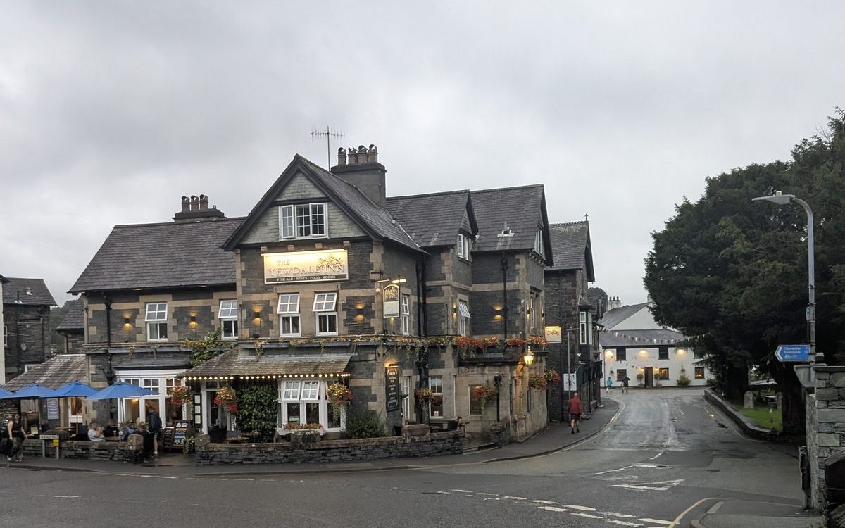 A slate-built inn on a corner in Coniston village with awnings over the ground floor, a road junction in front
