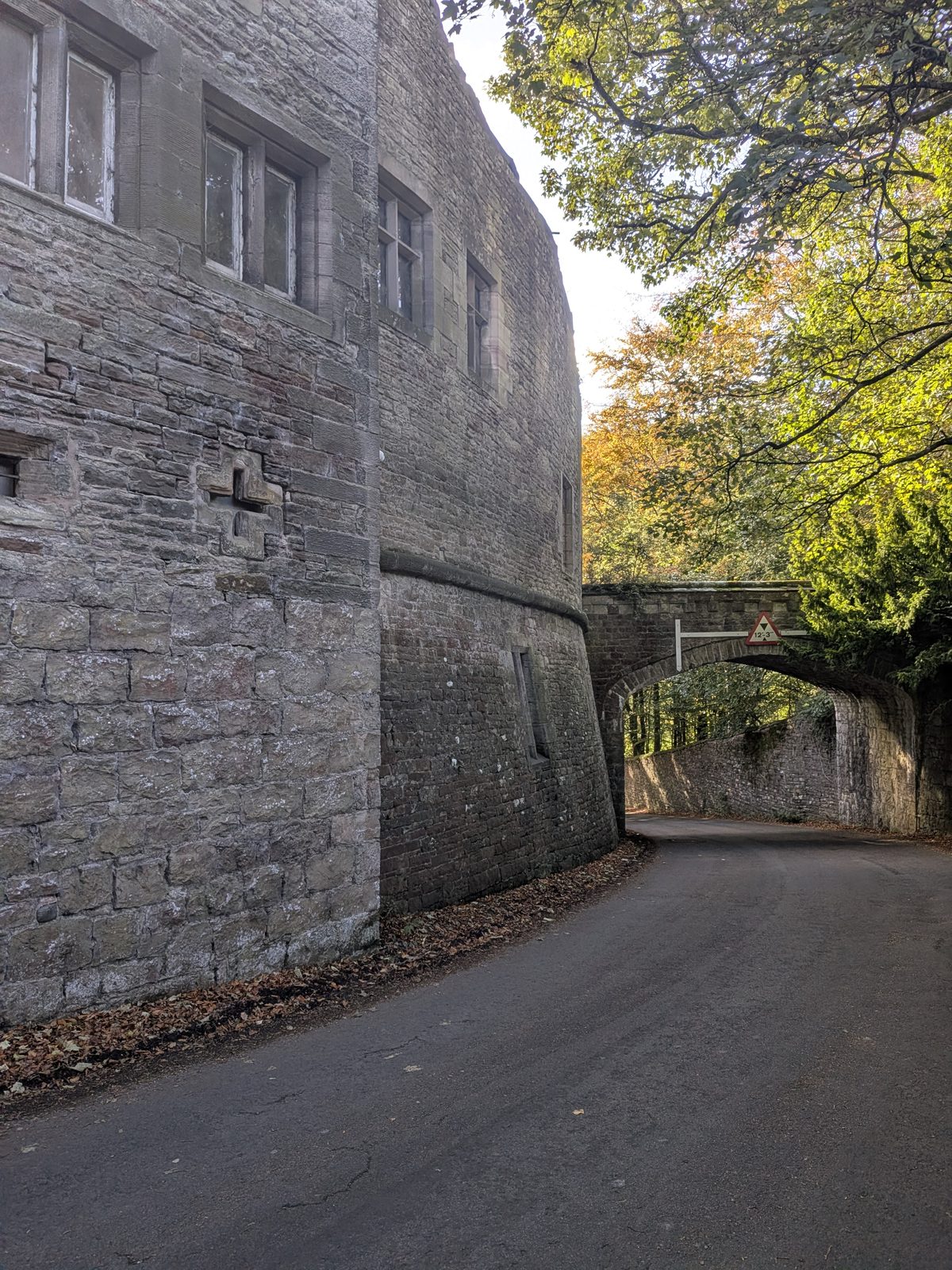 The high sandstone walls of Brougham Hall above the lane, with the arch beyond