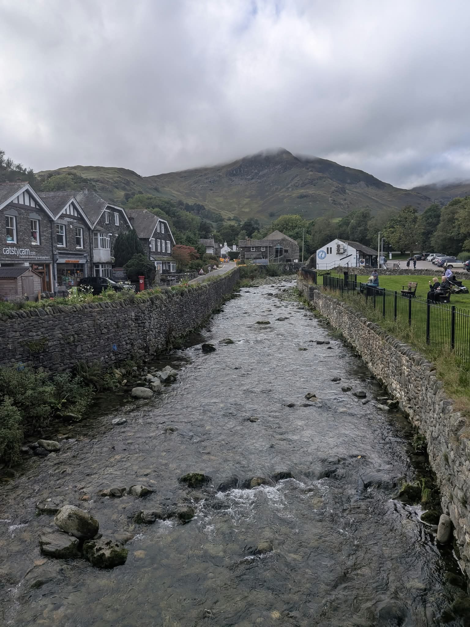 Glenridding Beck running between stone walls through the village, with the information centre on the right and the fells behind