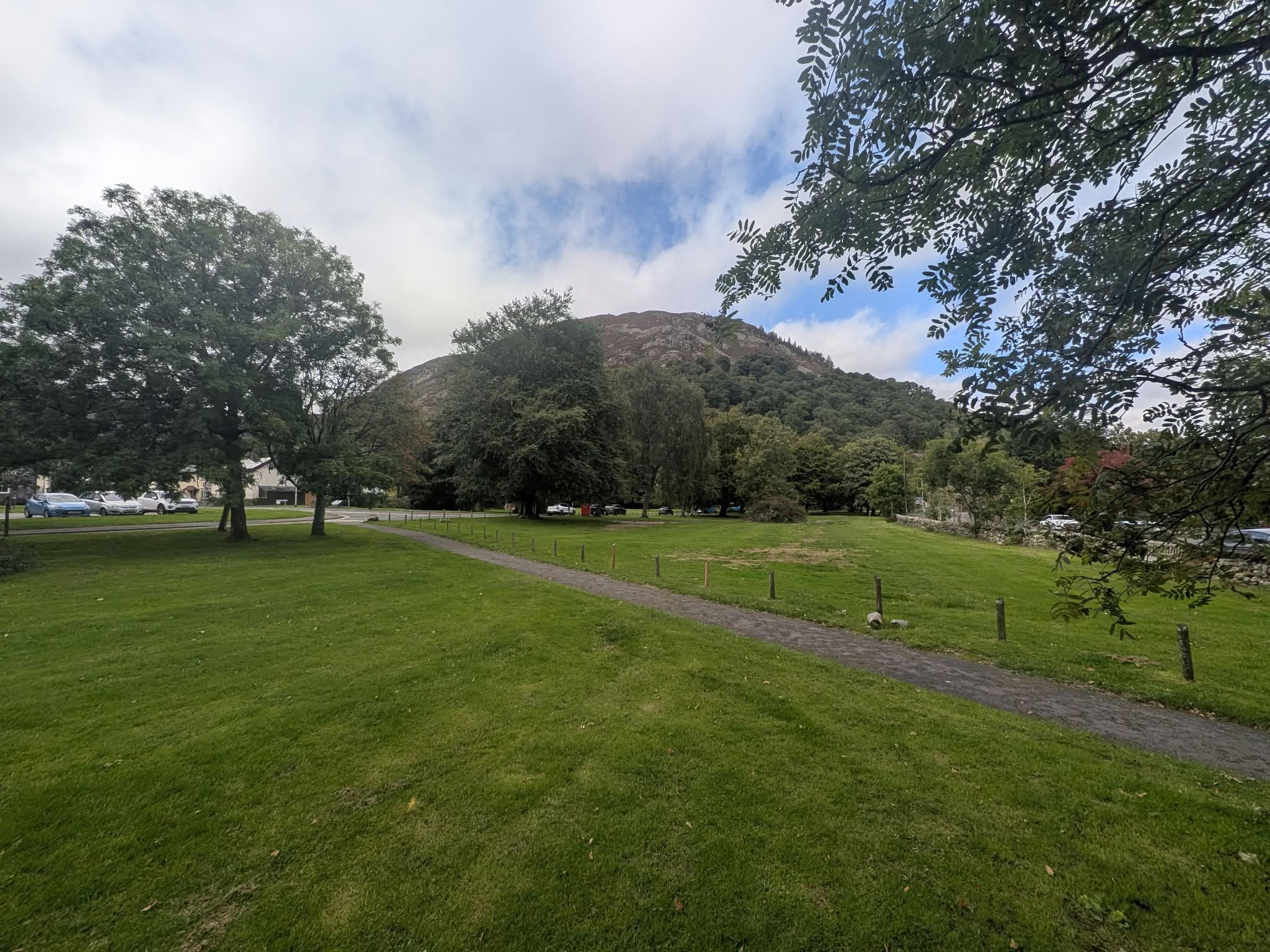 The village green at Glenridding, a path crossing the grass between trees with a wooded fell behind