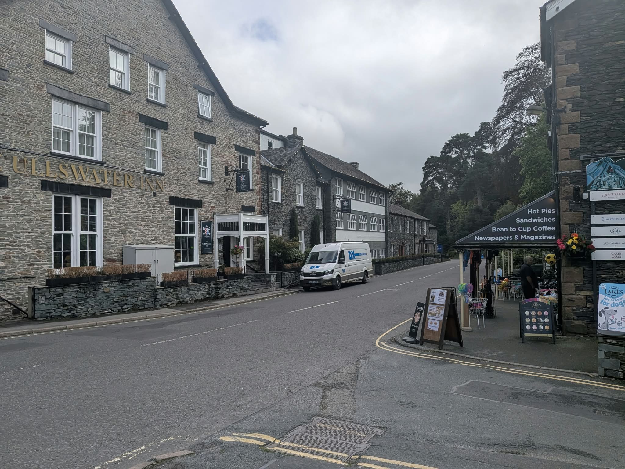The Ullswater Inn, a three-storey stone building, beside the village shop with its boards out on a quiet road in Glenridding