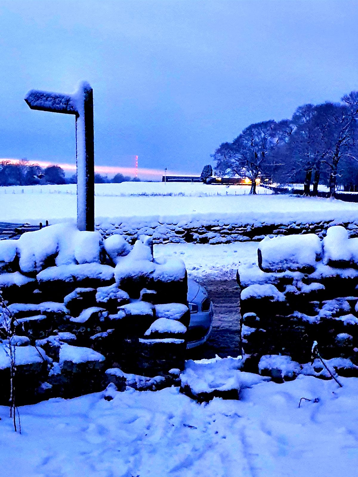 A snow-covered stile and footpath signpost at dusk on the Penrith evening circular