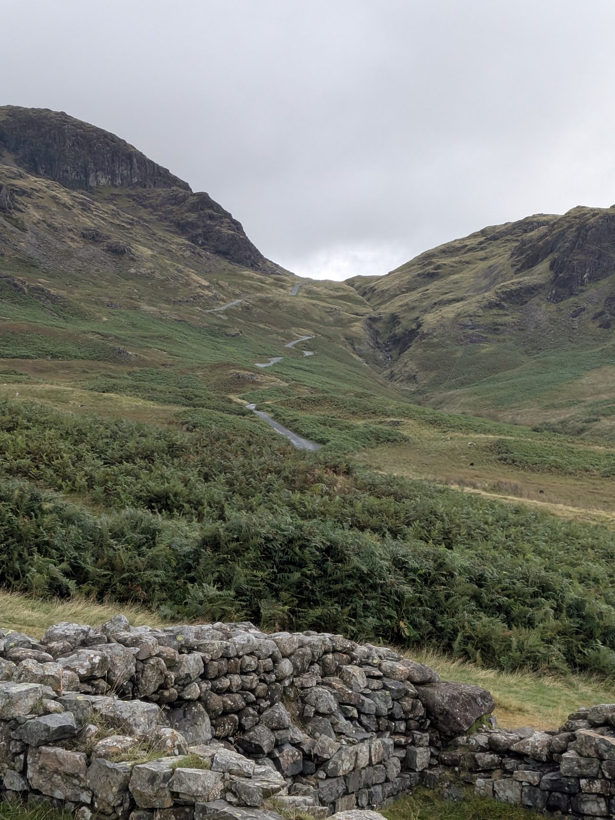 The Hardknott Pass road climbing in hairpins towards the summit, seen over the fort wall
