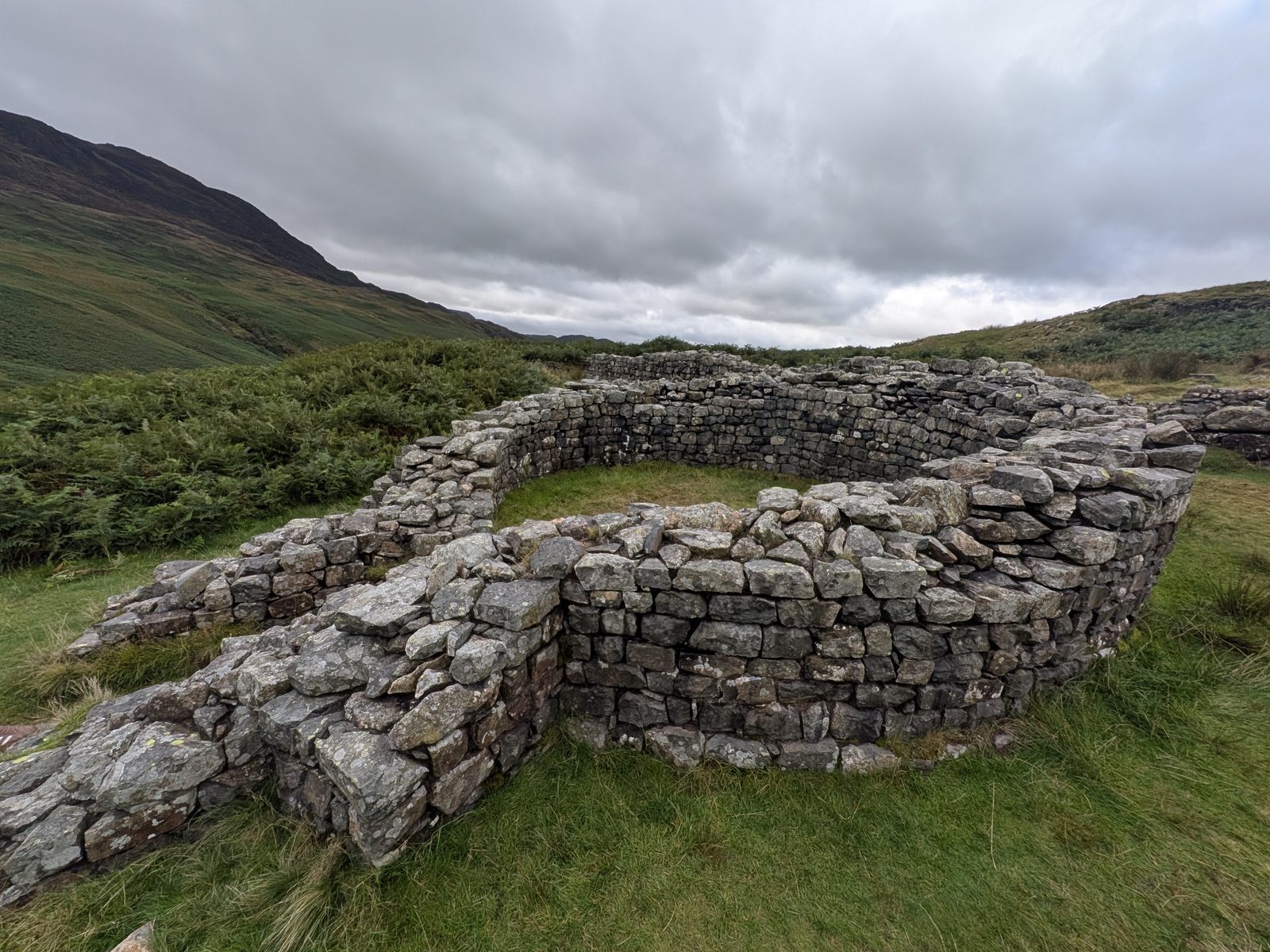 The circular stone walls of the laconicum, the dry sauna of the bath house at Hardknott Roman Fort, with the fellside behind