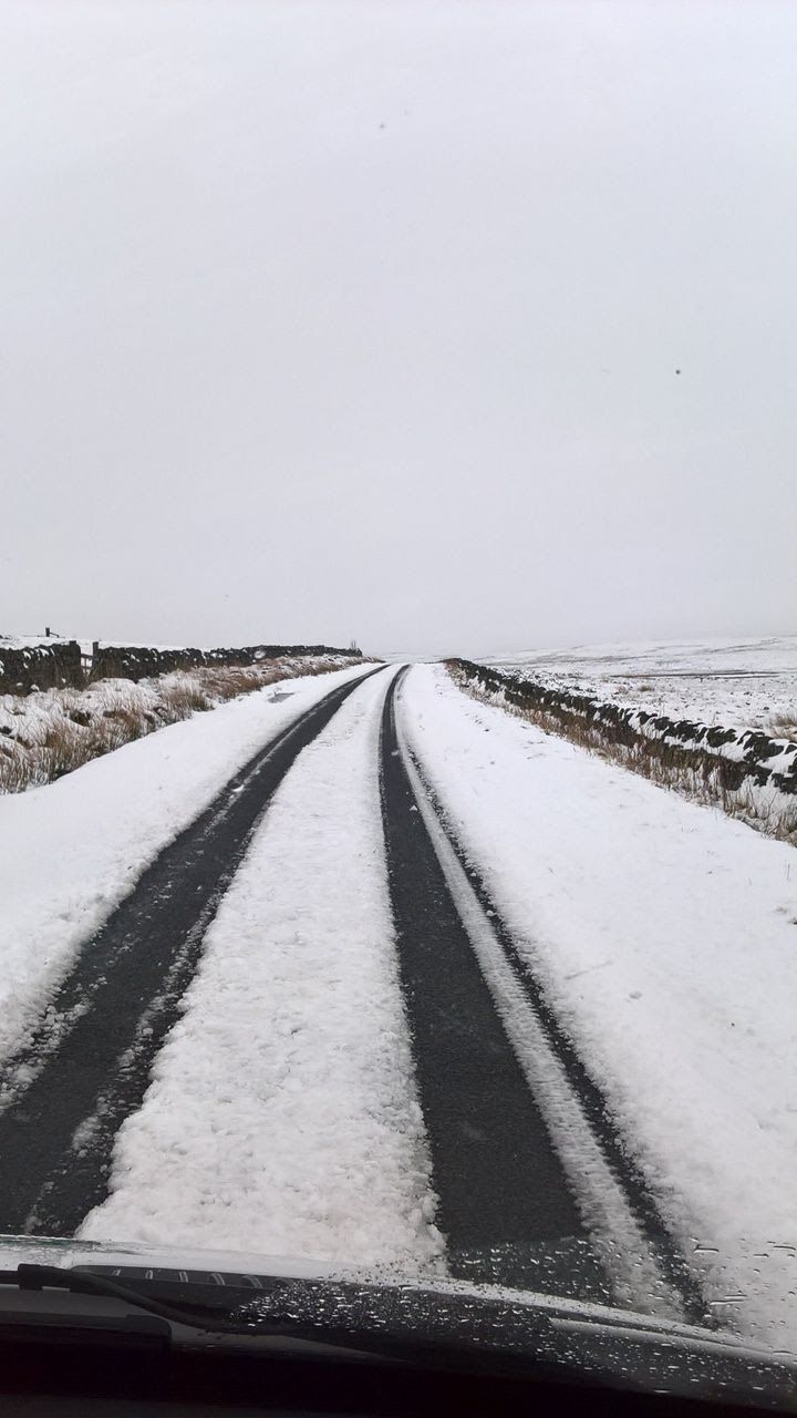 The snow-covered A686 with wheel tracks running between walls