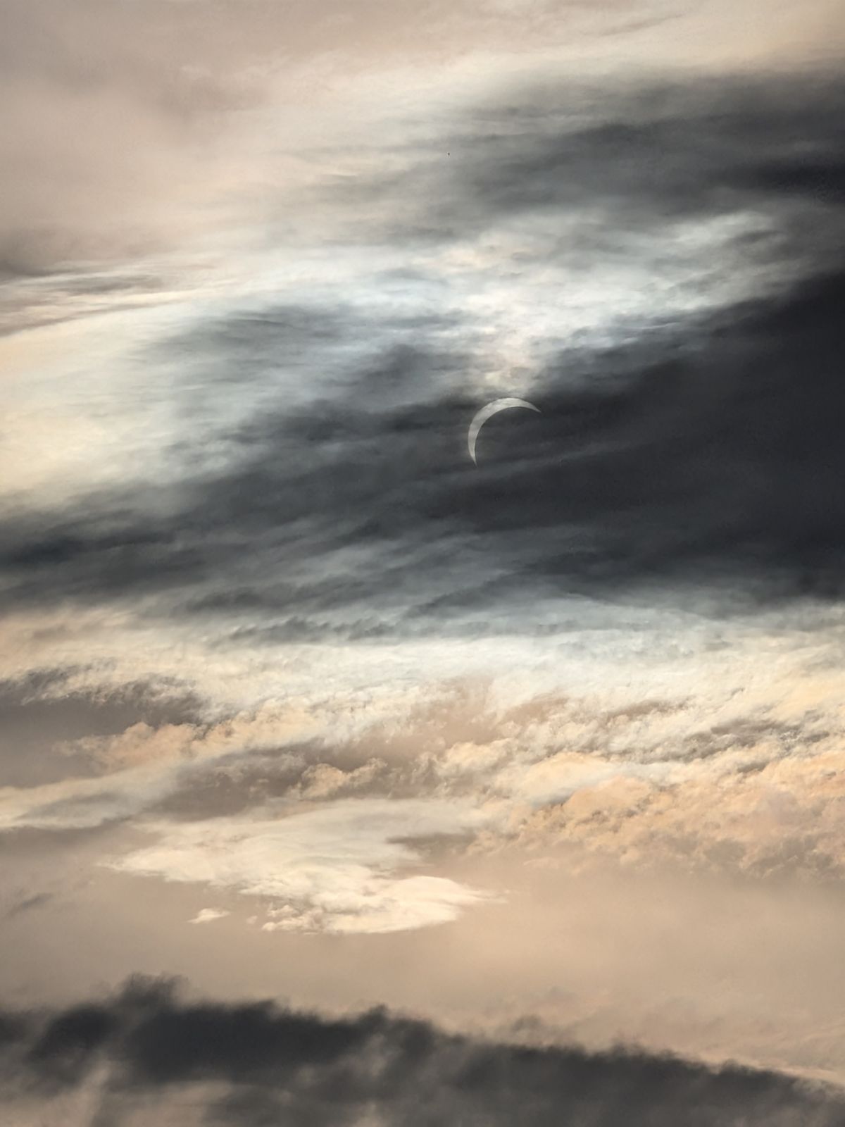 A thin crescent of the sun showing through broken cloud