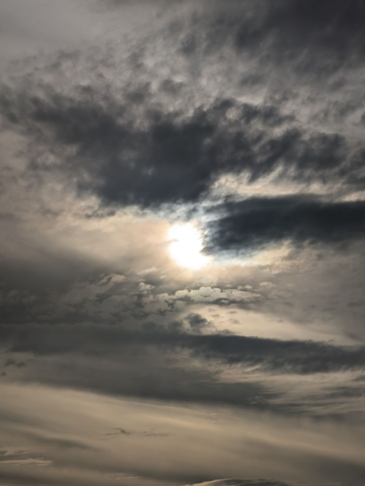The sun partly covered, seen through gaps in dark cloud