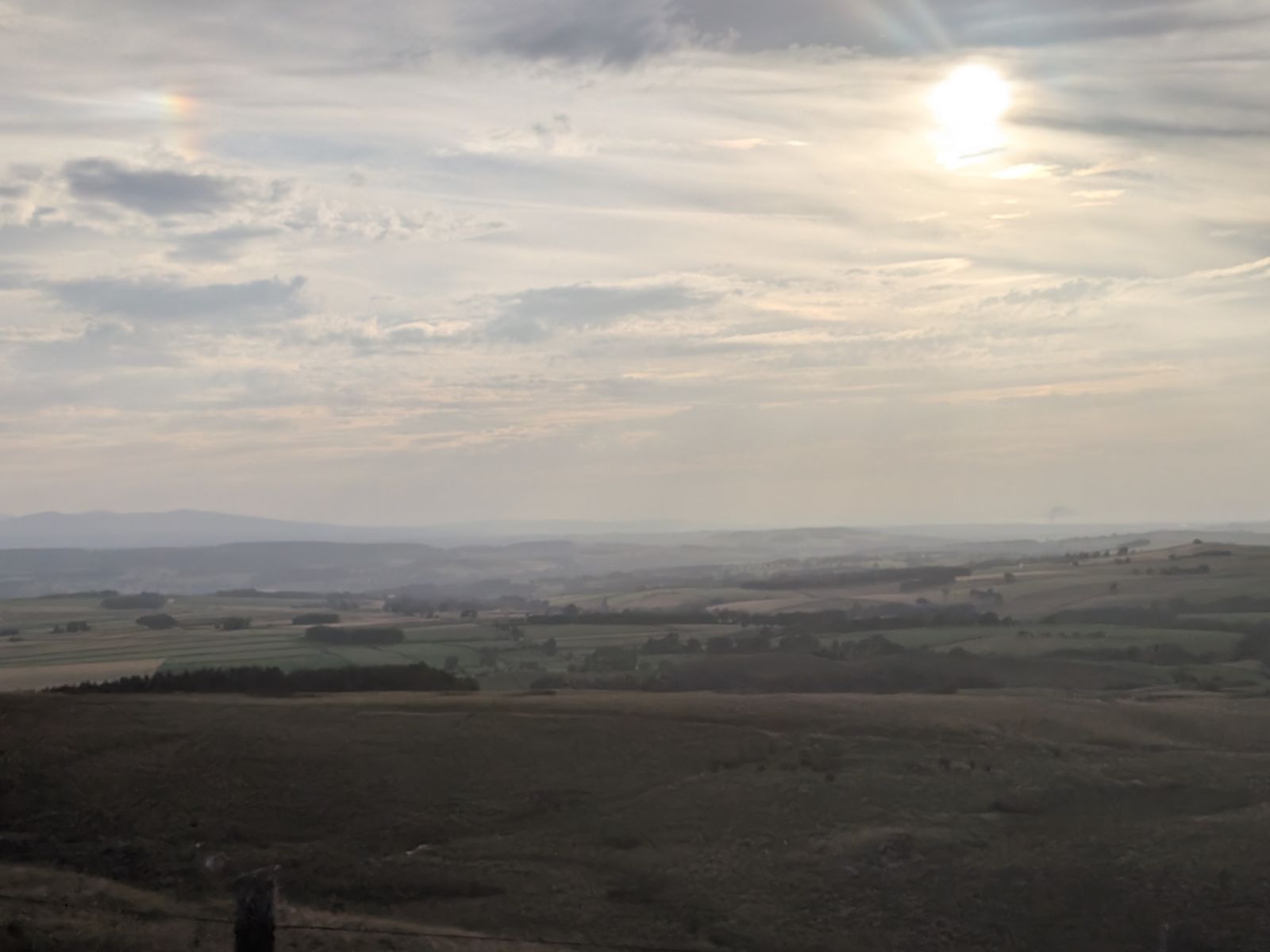 Moorland and fields below Hartside under a hazy sun, with a patch of rainbow light to its left