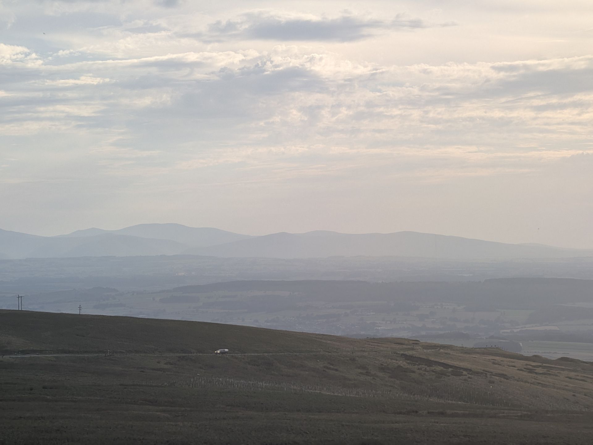 Moorland on Hartside with a single car on the road below, looking out over the layered Eden Valley to distant hills in evening haze