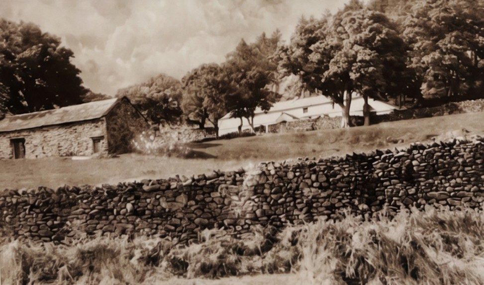 Old sepia photograph of Low Whelter farm, Mardale: low stone farm buildings among trees on a fellside, with a drystone wall in the foreground