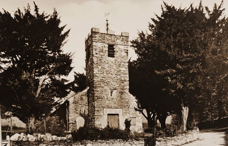 Old sepia photograph of Holy Trinity church at Mardale Green: a squat stone tower with a small turret, half hidden among tall dark trees