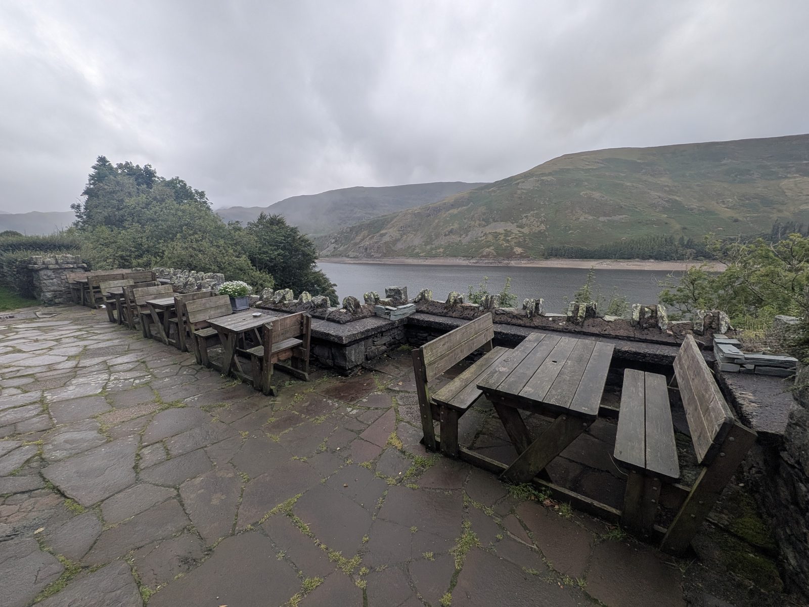 The flagged terrace of the Haweswater Hotel with wooden picnic benches, looking down the length of the reservoir to the fells at its head under low cloud