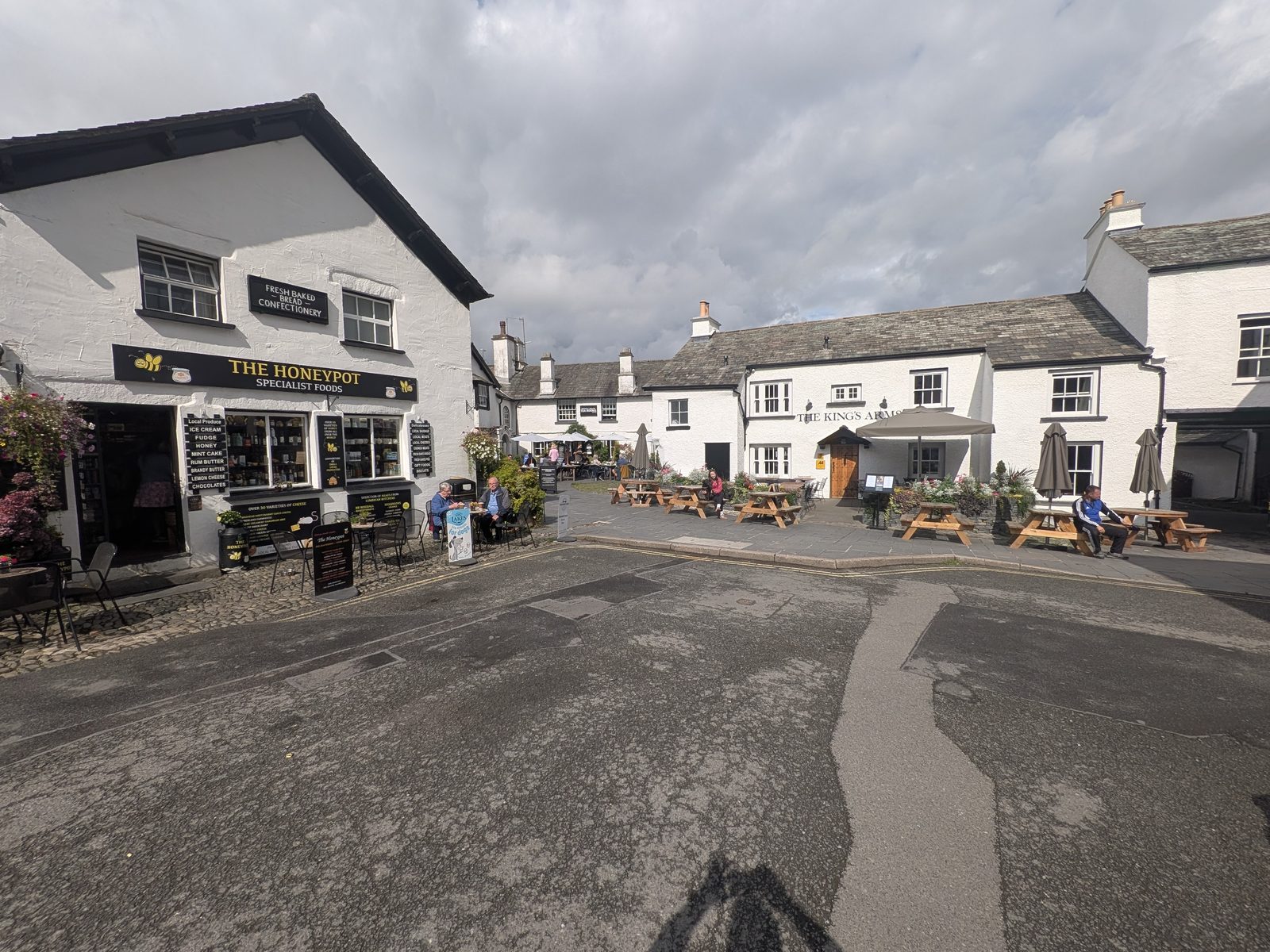 The village square at Hawkshead, whitewashed and slate-roofed buildings around the open cobbled centre with picnic benches outside, Lake District