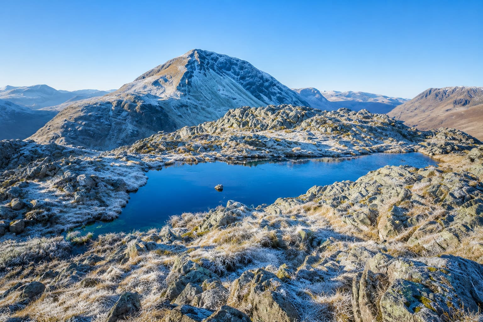 A small tent pitched on the Lake District high fells at dusk beside a mountain tarn
