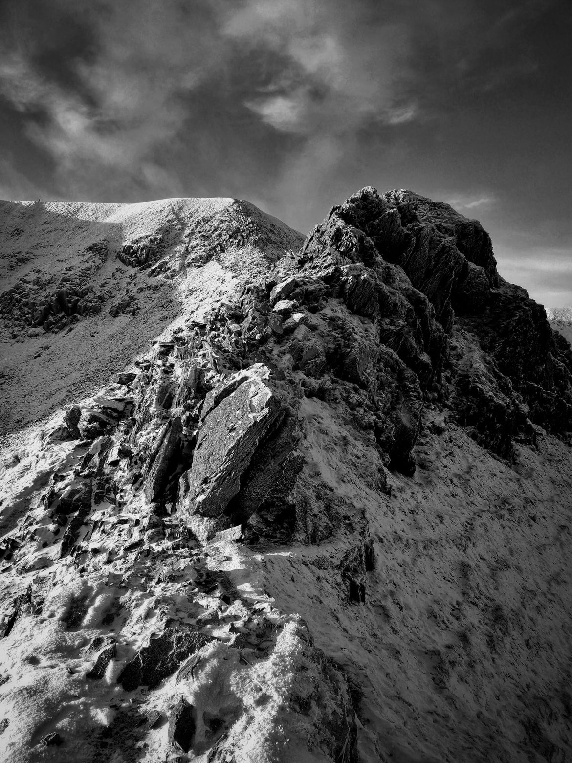 Black and white view along a snow-covered rocky ridge on Helvellyn under a dark winter sky