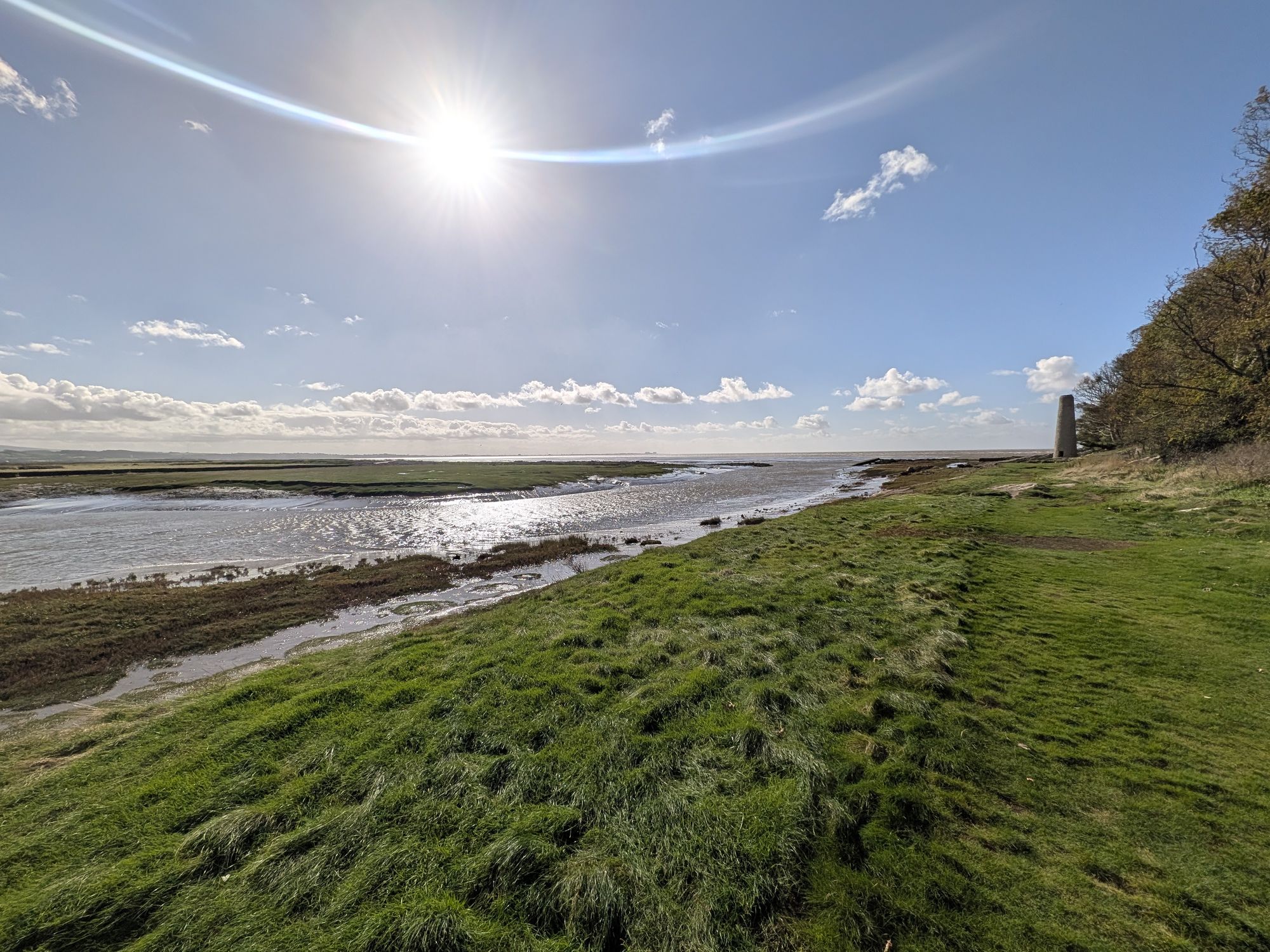 The stone chimney at Jenny Brown's Point at the edge of the saltmarsh, with a tidal channel and Morecambe Bay under a bright sun