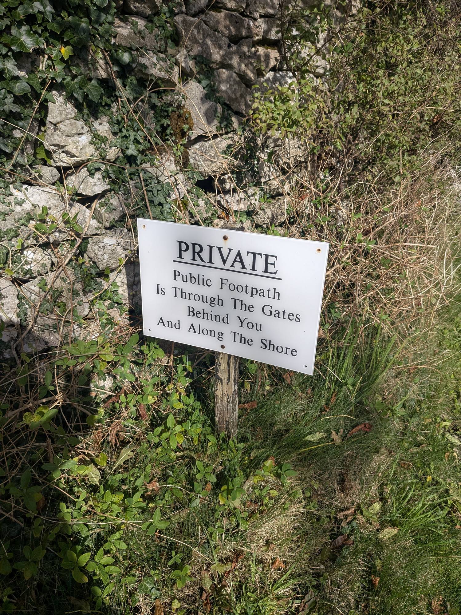 White sign reading Private, Public Footpath Is Through The Gates Behind You And Along The Shore