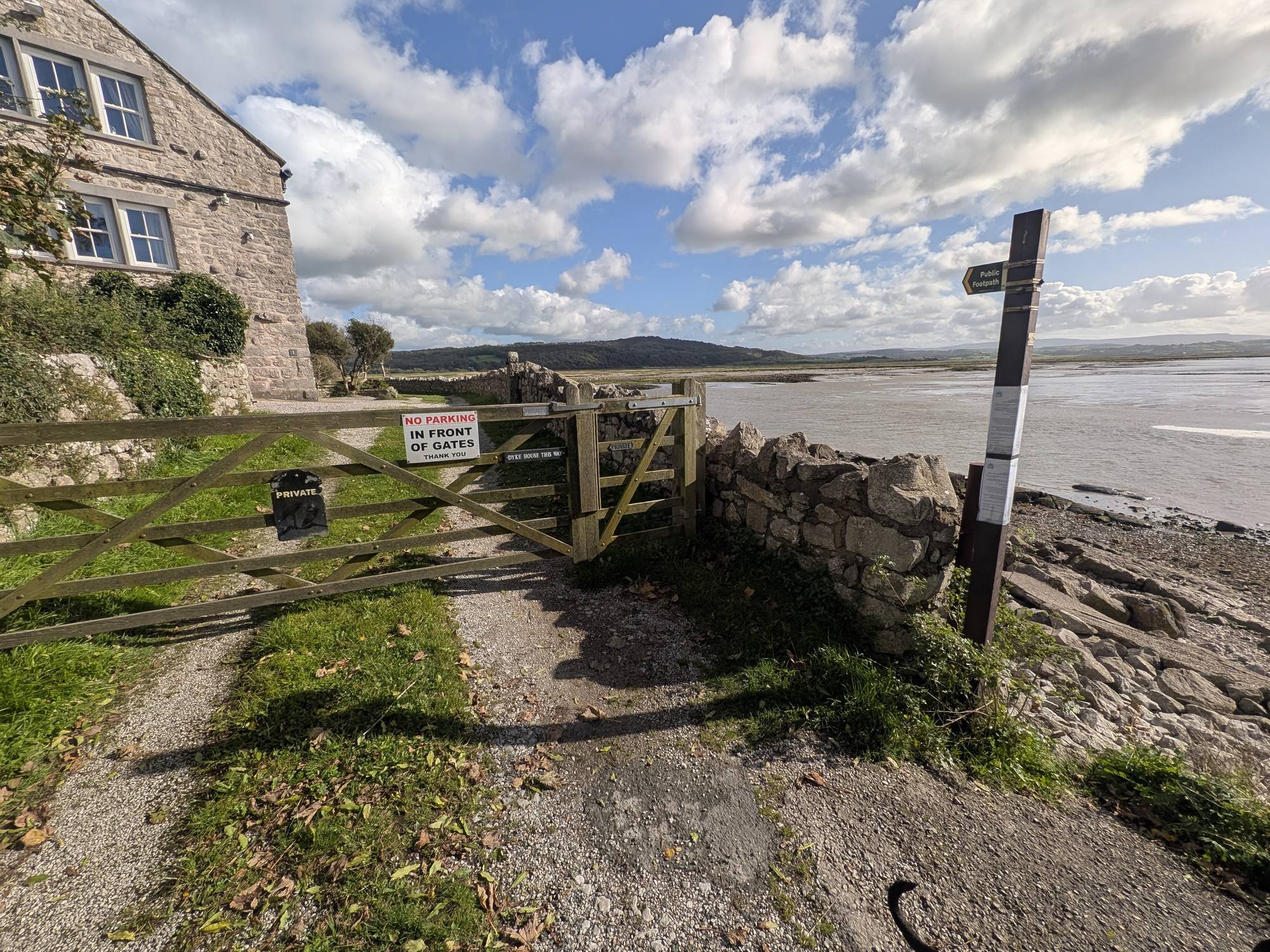 A five-bar gate marked Private and No Parking in Front of Gates beside a stone house, with a public footpath fingerpost and the estuary to the right