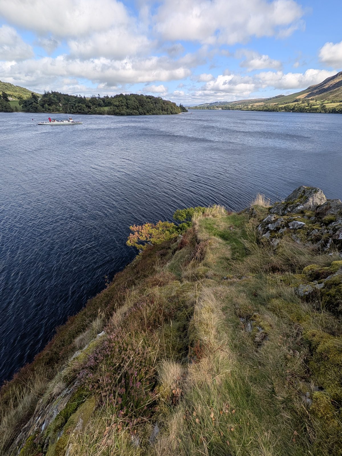 Steep grass and rock at the edge of Kailpot Crag dropping straight into deep water, an Ullswater Steamer on the lake beyond