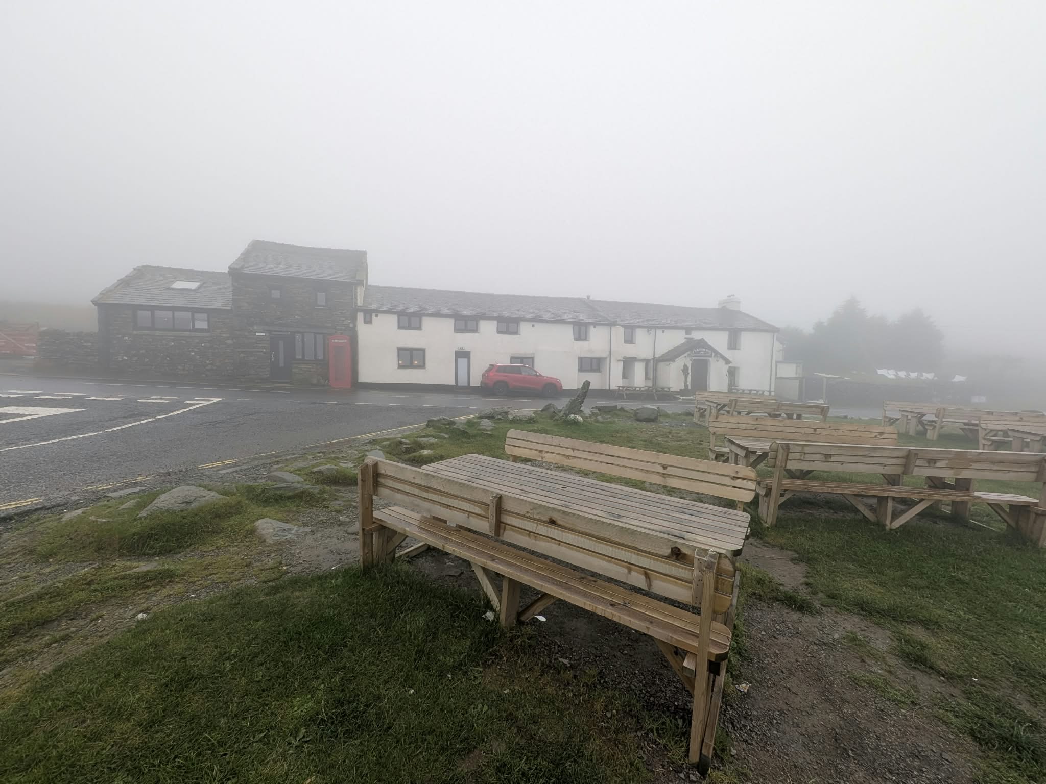 The Kirkstone Pass Inn in thick mist, with empty wooden picnic benches on the grass in front