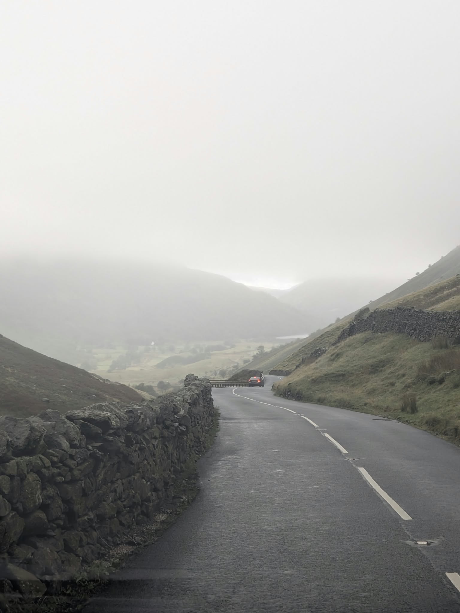 The A592 dropping away from Kirkstone Pass on the Ullswater side, between stone walls, with the valley lost in mist