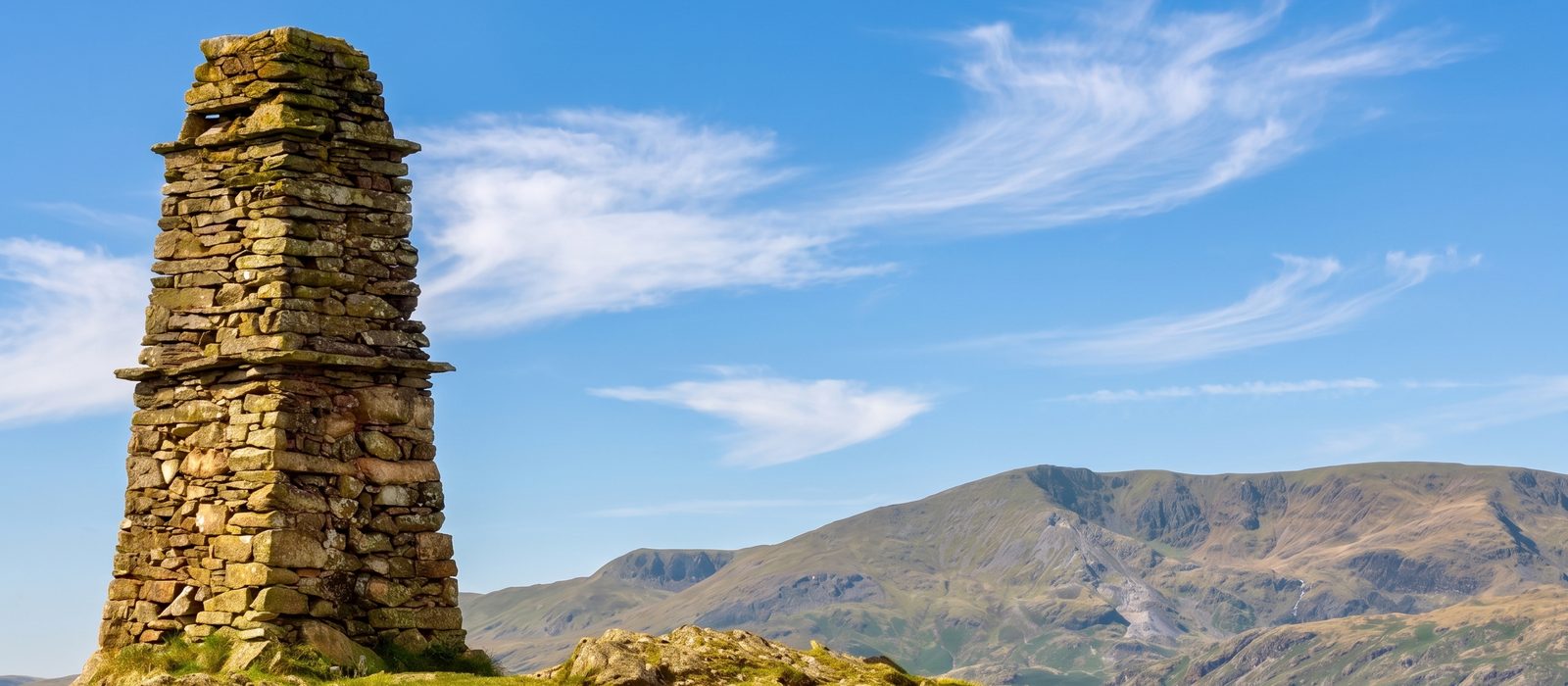 The stone cairn on the summit of Latterbarrow with the fells beyond, near Hawkshead, Lake District