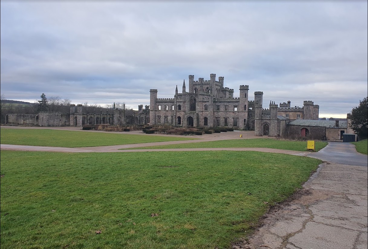 The full width of Lowther Castle's ruined garden front across open lawn, with the converted stable block to one side