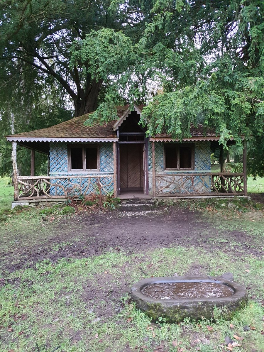 A timber summerhouse in the gardens at Lowther Castle, with a deep overhanging roof and rustic branchwork railings