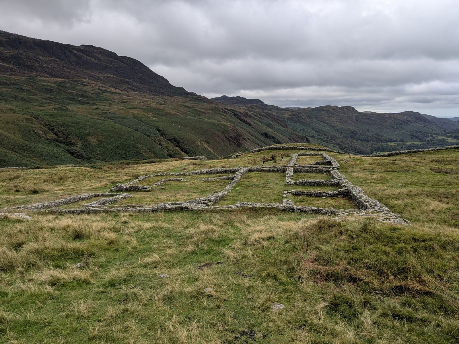 Stone wall footings of buildings inside Hardknott Roman Fort, with the fort wall beyond and Eskdale falling away to the right