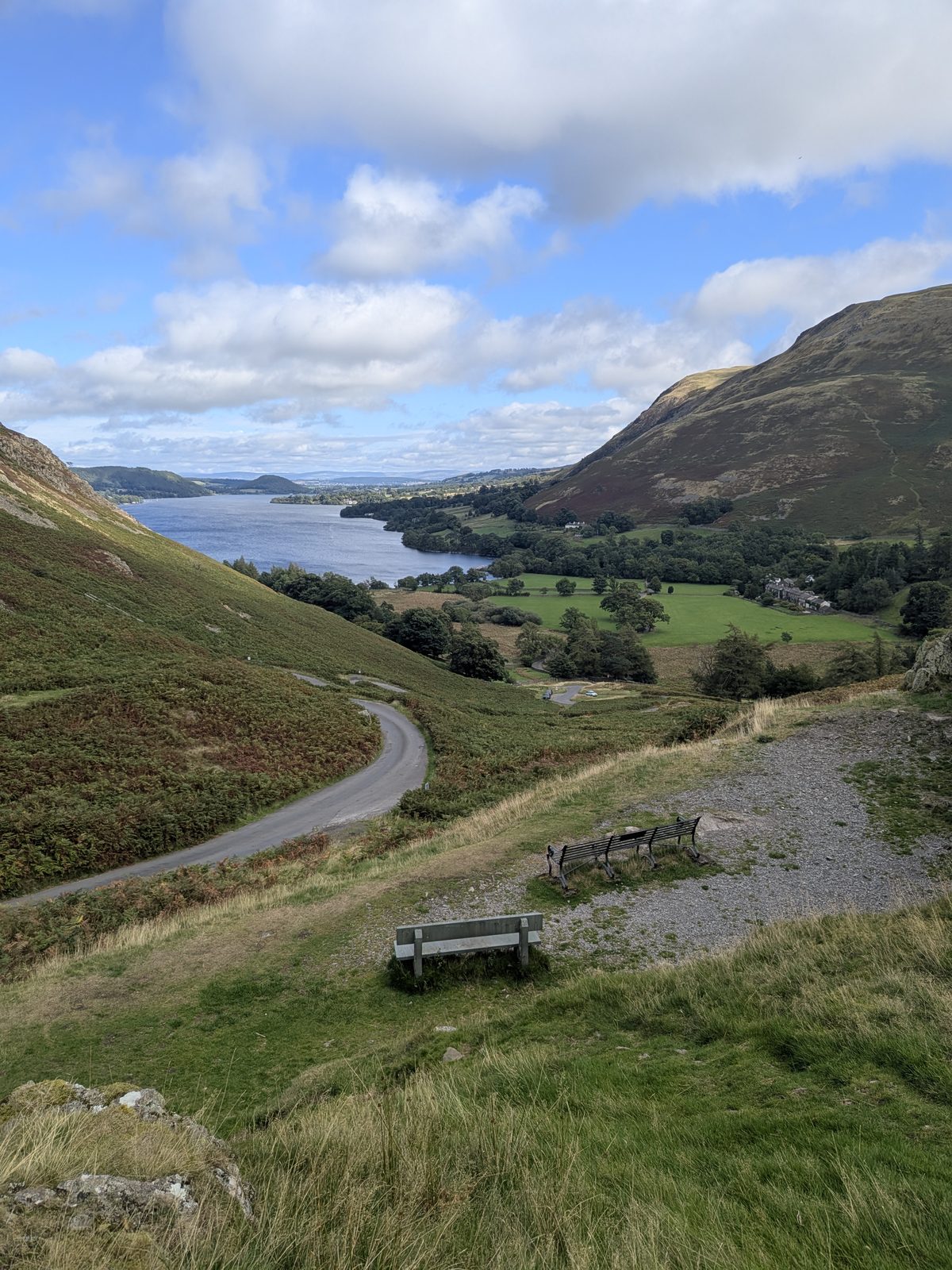 The road dropping in bends from the Hause at Martindale towards Howtown, benches in the foreground and Ullswater beyond
