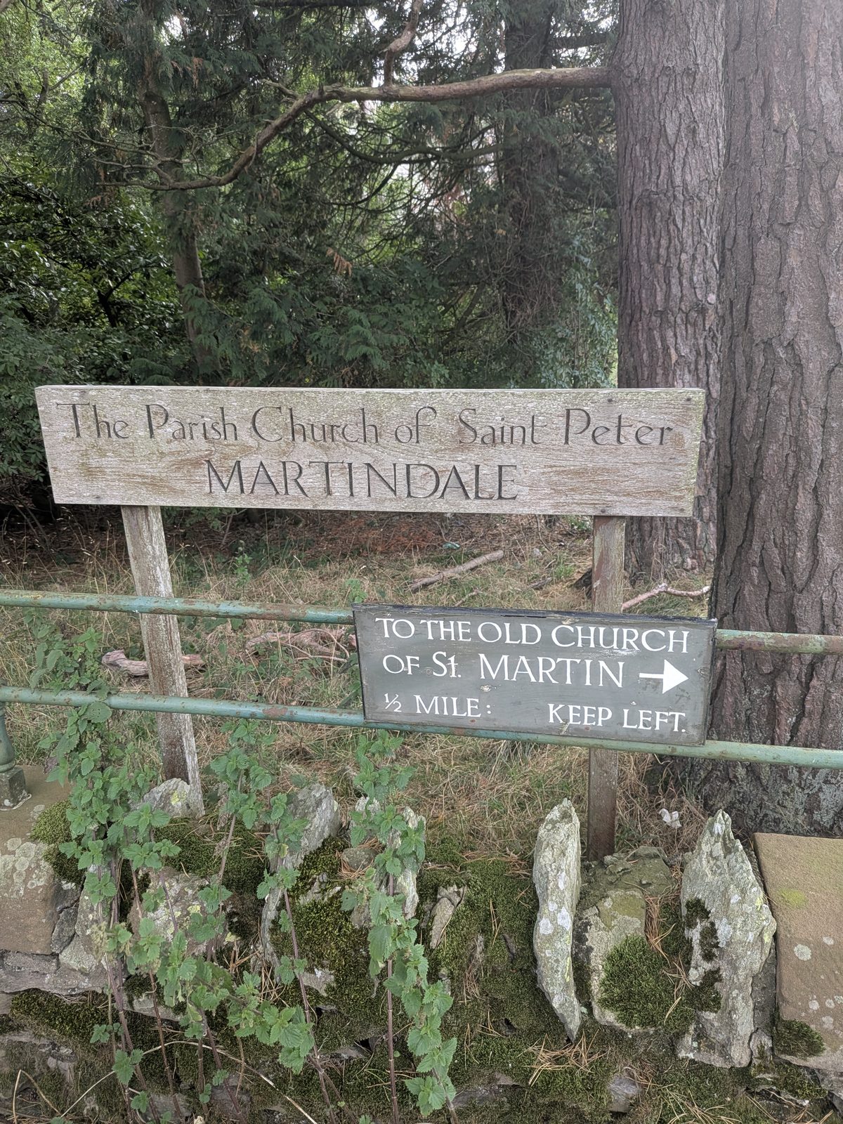 The sign for The Parish Church of Saint Peter, Martindale, with a direction board beneath it pointing to St Martin's Old Church half a mile away